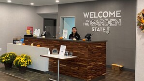 A reception desk with a wooden design, a welcome sign, and a framed certificate. There are potted plants and a small table with a sign and a phone. - Hampton Inn Egg Harbor Township Atlantic City (Egg Harbor Township)