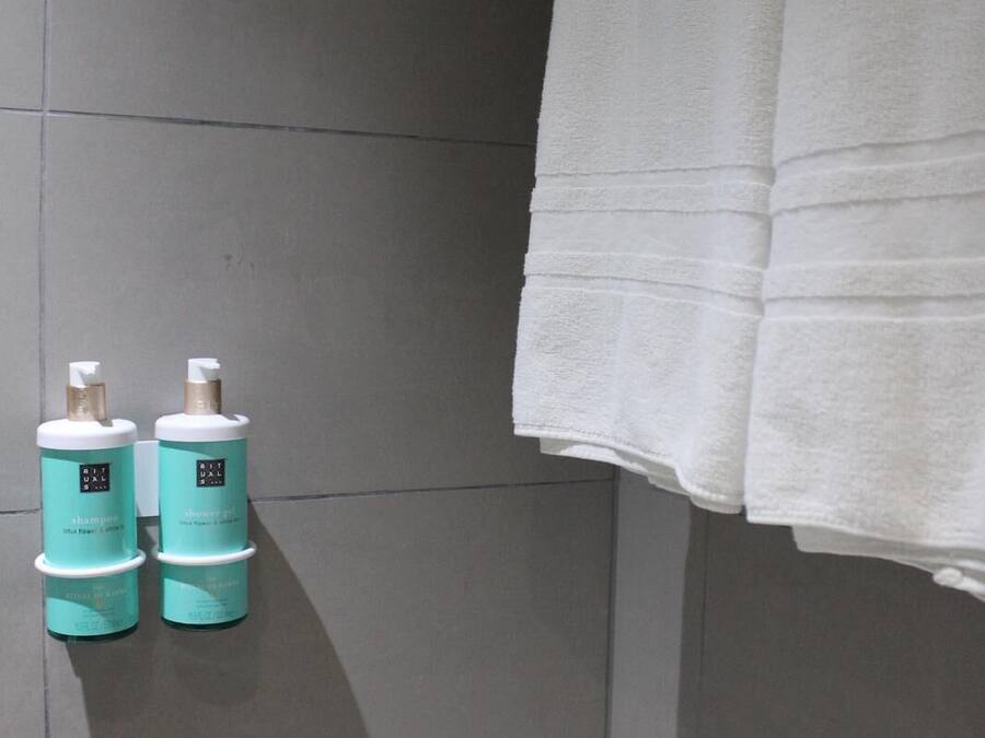 A bathroom with grey tiles, two bottles of shampoo and shower gel, and a white towel hanging on the wall.