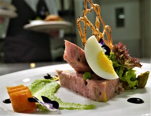 A plated dish with various food items including a slice of meat, a boiled egg, and some greens. - Novotel London Stansted Airport (Stansted)