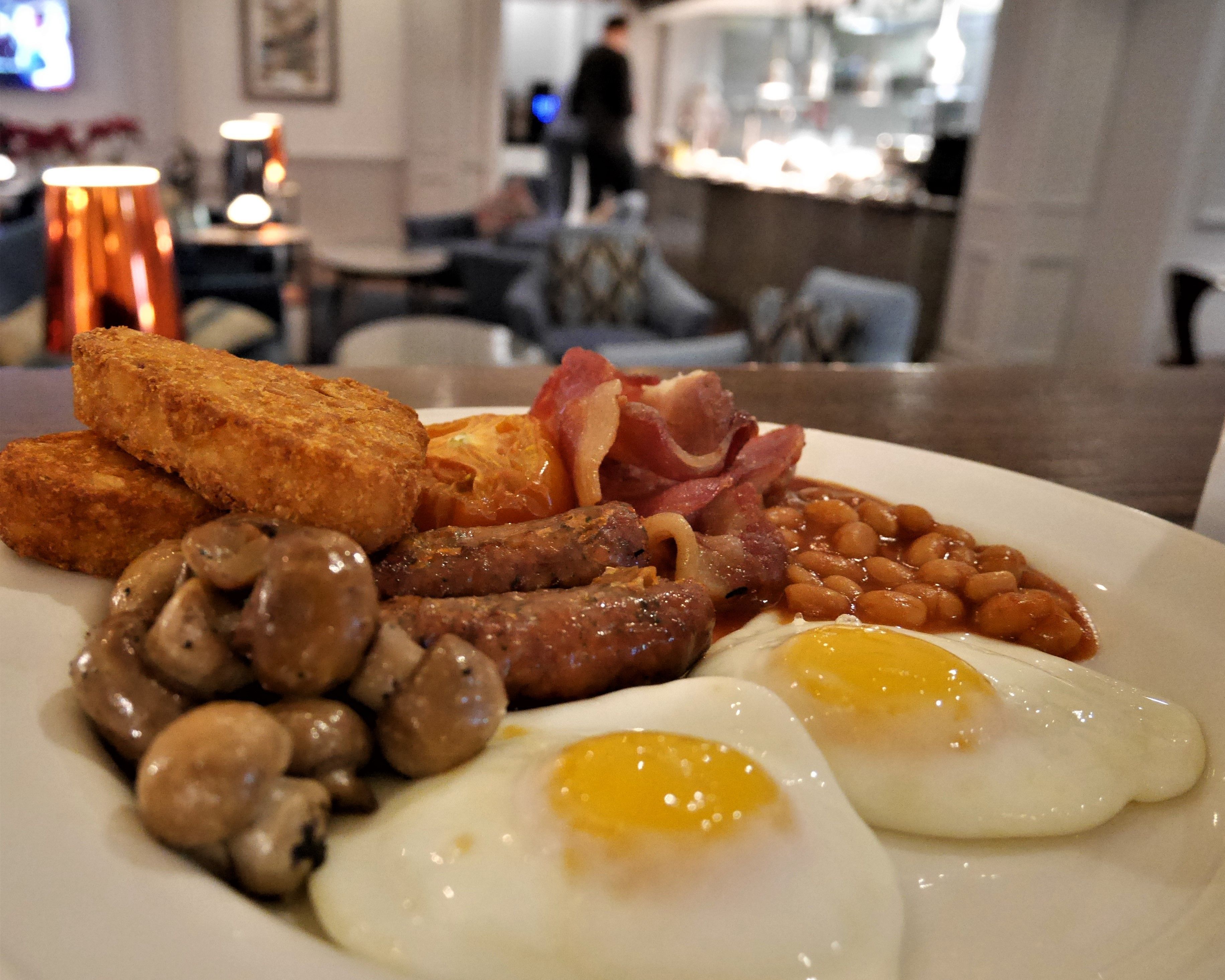A breakfast plate with eggs, sausages, mushrooms, beans, bacon, and fried bread.