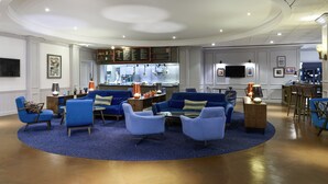 Amplia sala de estar con sofás azules, una mesa de centro y una cocina al fondo.