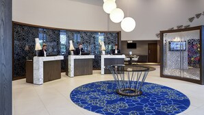 Un área de recepción moderna con mostradores de mármol, alfombra estampada en azul y lámparas esféricas colgantes.