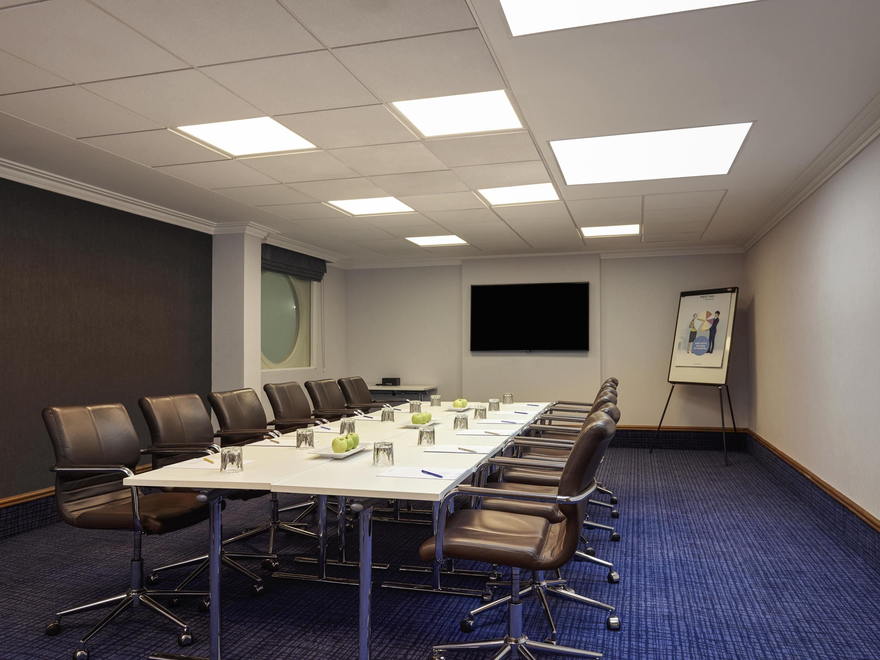 A conference room with a long table, chairs, a projector screen, and a flip chart.