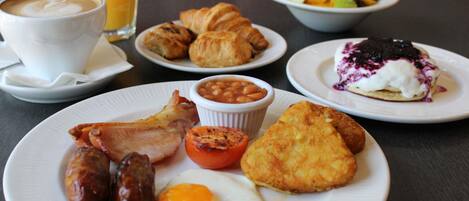 Una mesa de desayuno con platos de comida, incluyendo salchichas, tocino, huevos y pastelería.