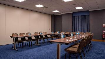 Une salle de conférence avec de longues tables, des chaises, des bouteilles d’eau et un extincteur.