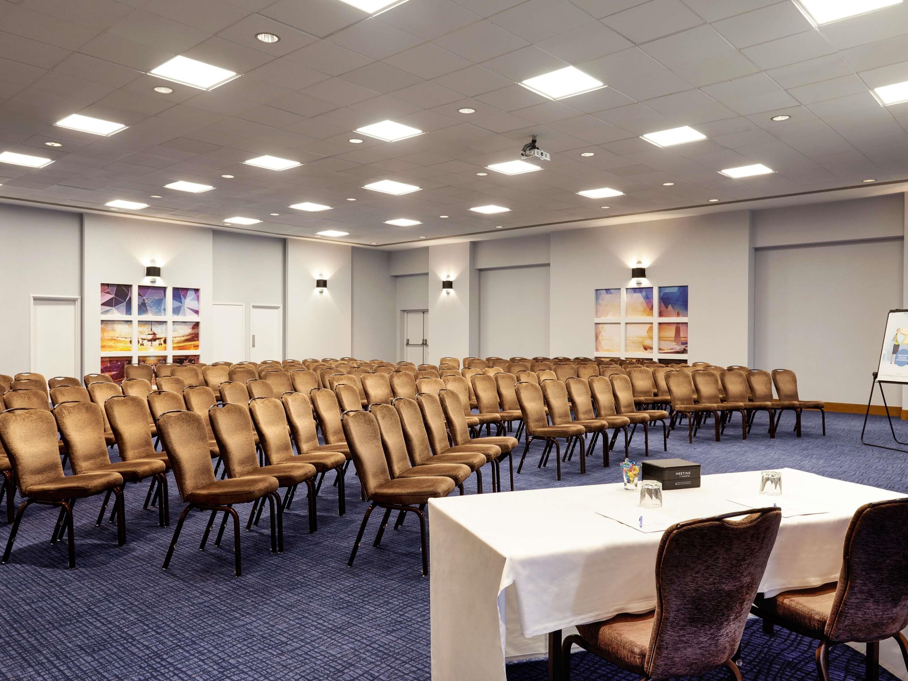 A conference room with rows of chairs, a white table, and a projector screen.