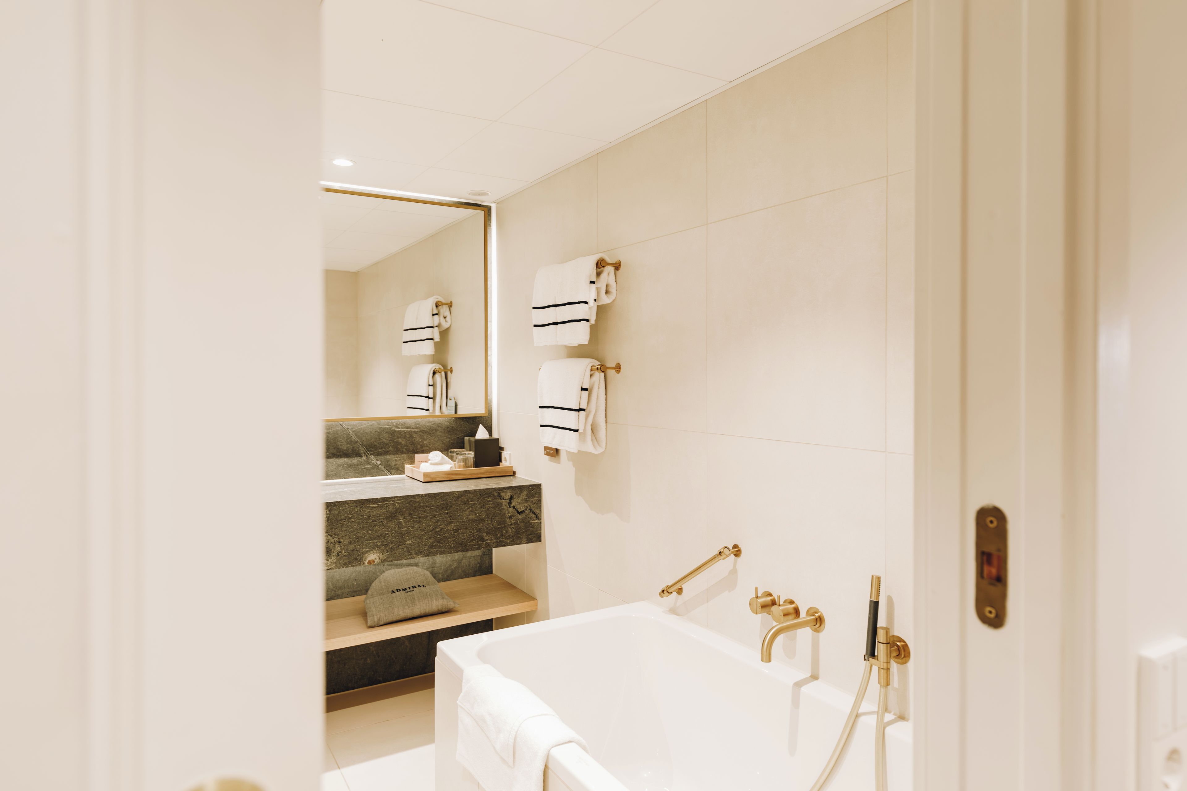 A modern bathroom with a large mirror, a bathtub, and a vanity with a marble countertop.