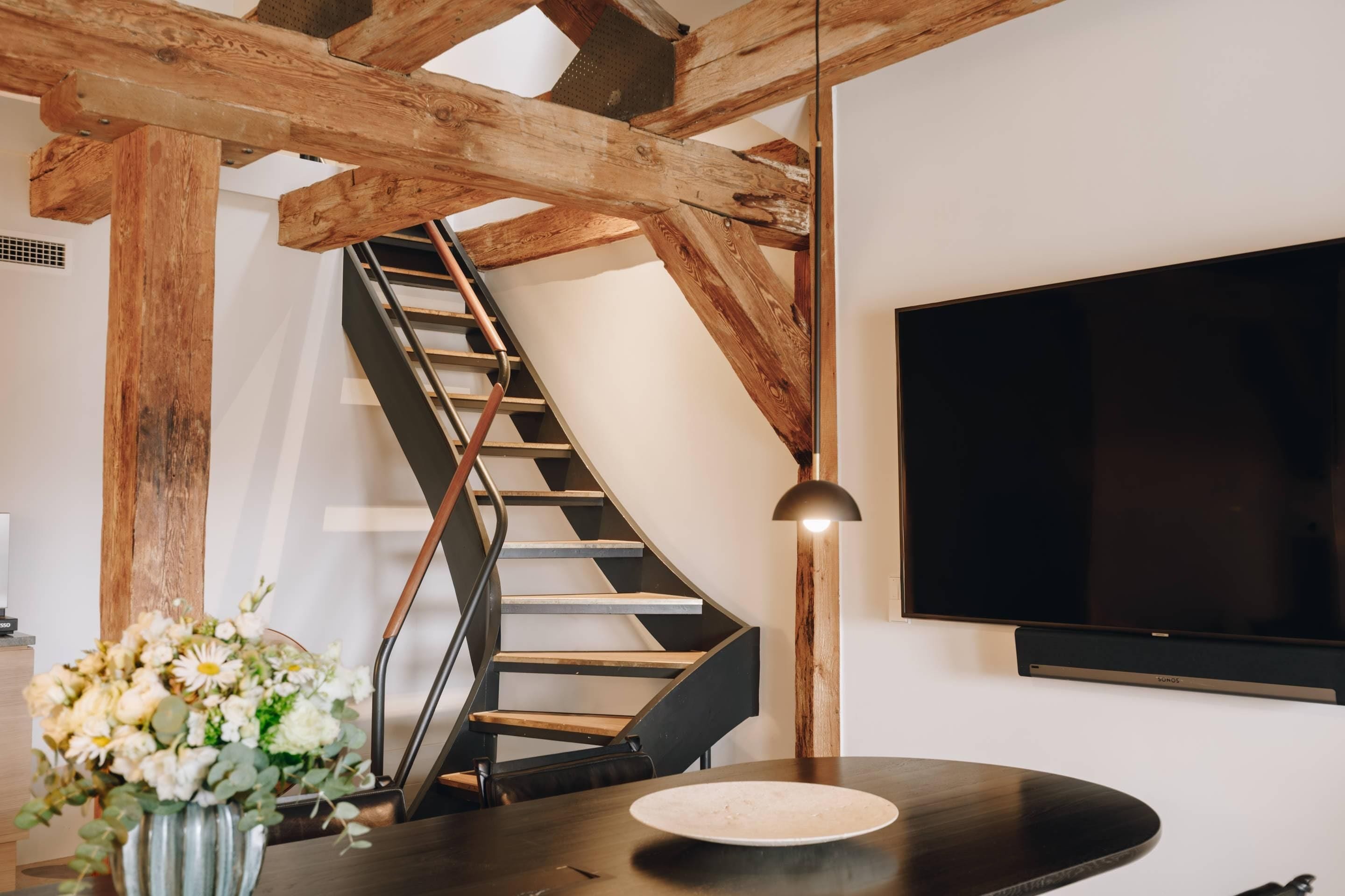 A modern interior with a curved staircase, a flat-screen TV, and a minimalist dining area.