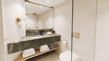 Uma casa de banho moderna com bancada de mármore, um espelho grande, sanita e cabine de duche com paredes de vidro.