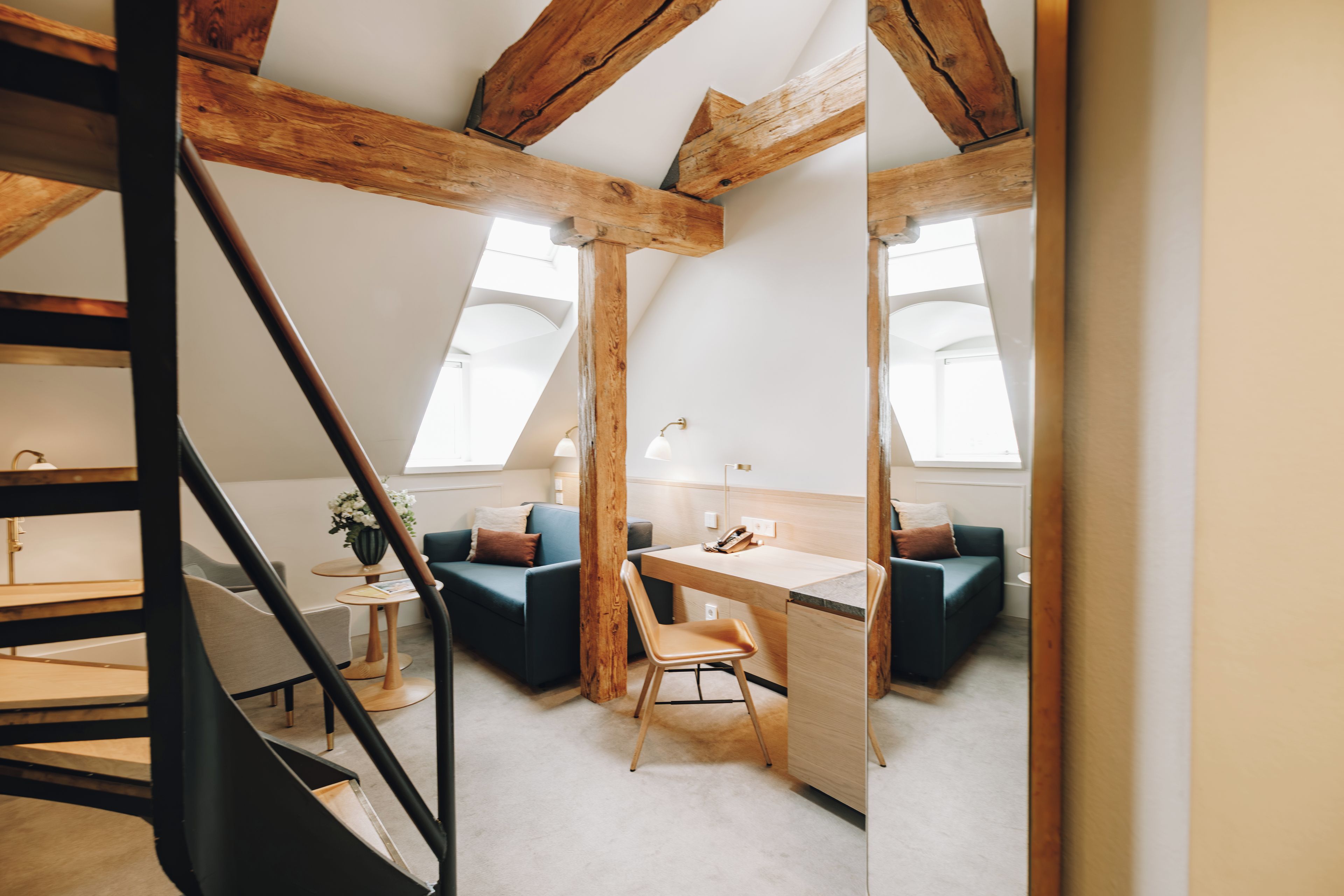 Un dormitorio tipo loft moderno con techo inclinado, una escalera de madera, un escritorio y una zona de estar cómoda.