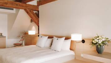 Un dormitorio con techo de madera, una cama con ropa blanca, una mesita de noche con lámpara y un jarrón con flores.