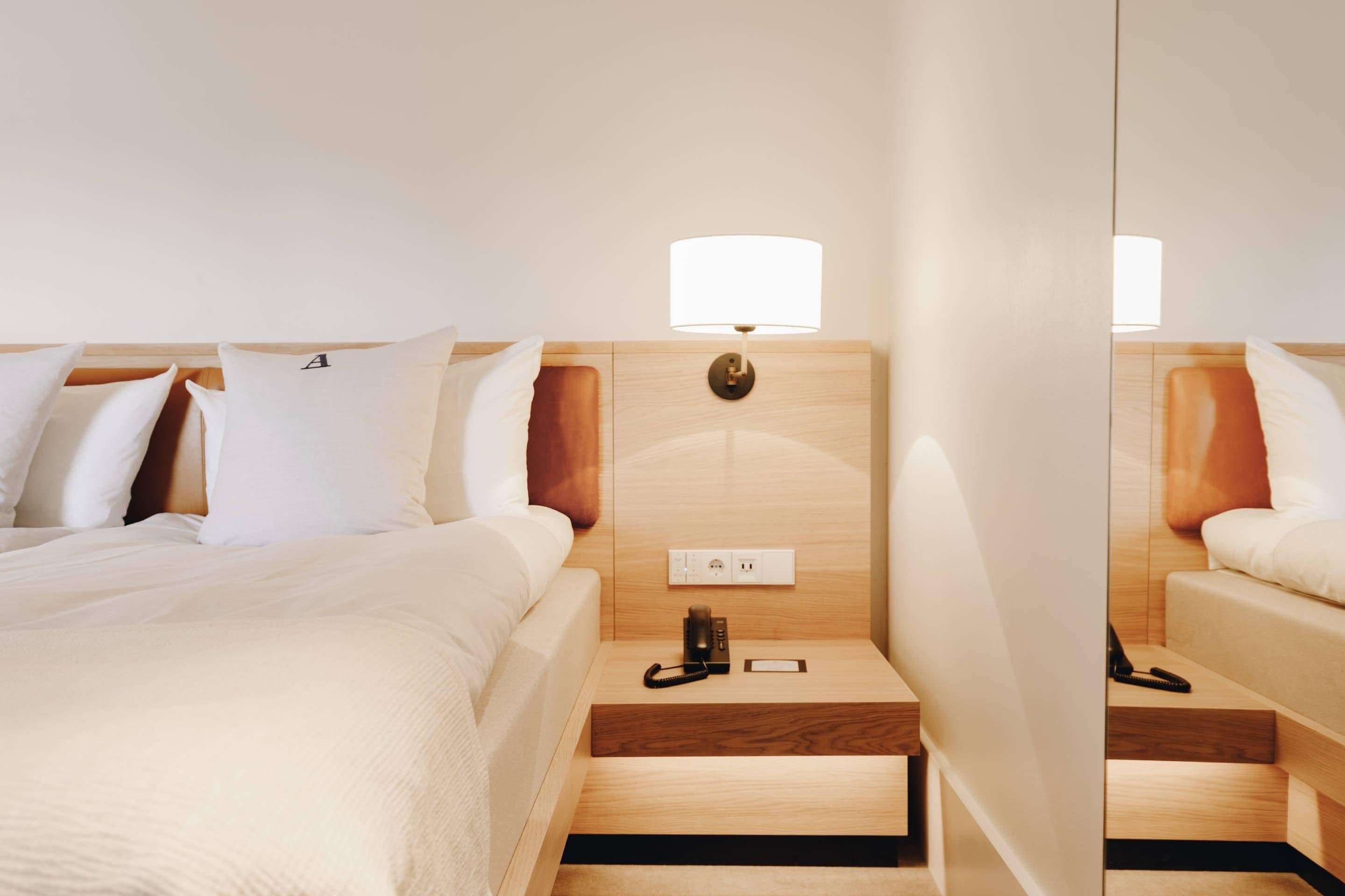A hotel room with a bed, bedside tables, a lamp, and a mirror.