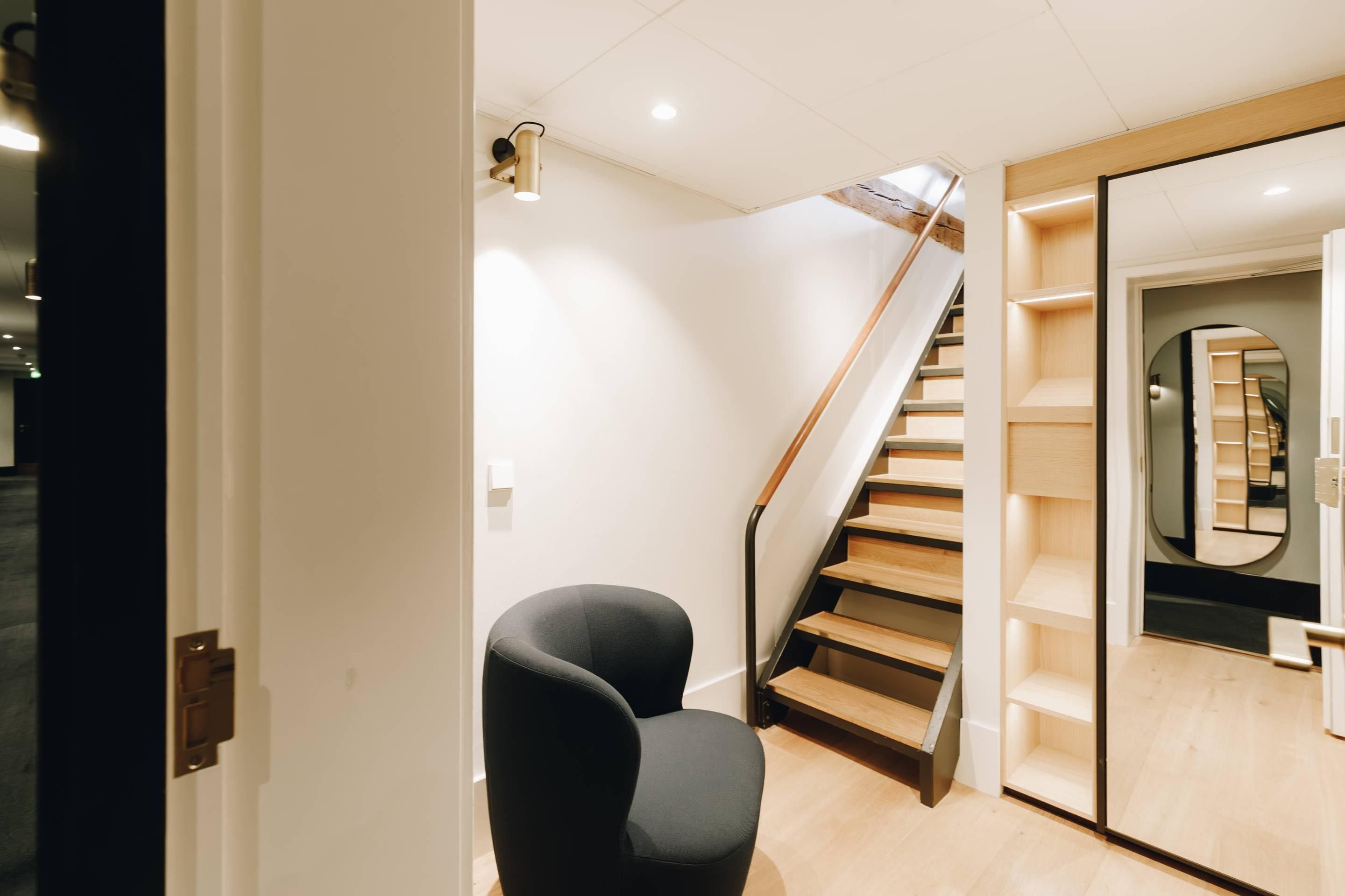 Un intérieur moderne avec un escalier, une chaise noire et un plancher en bois.