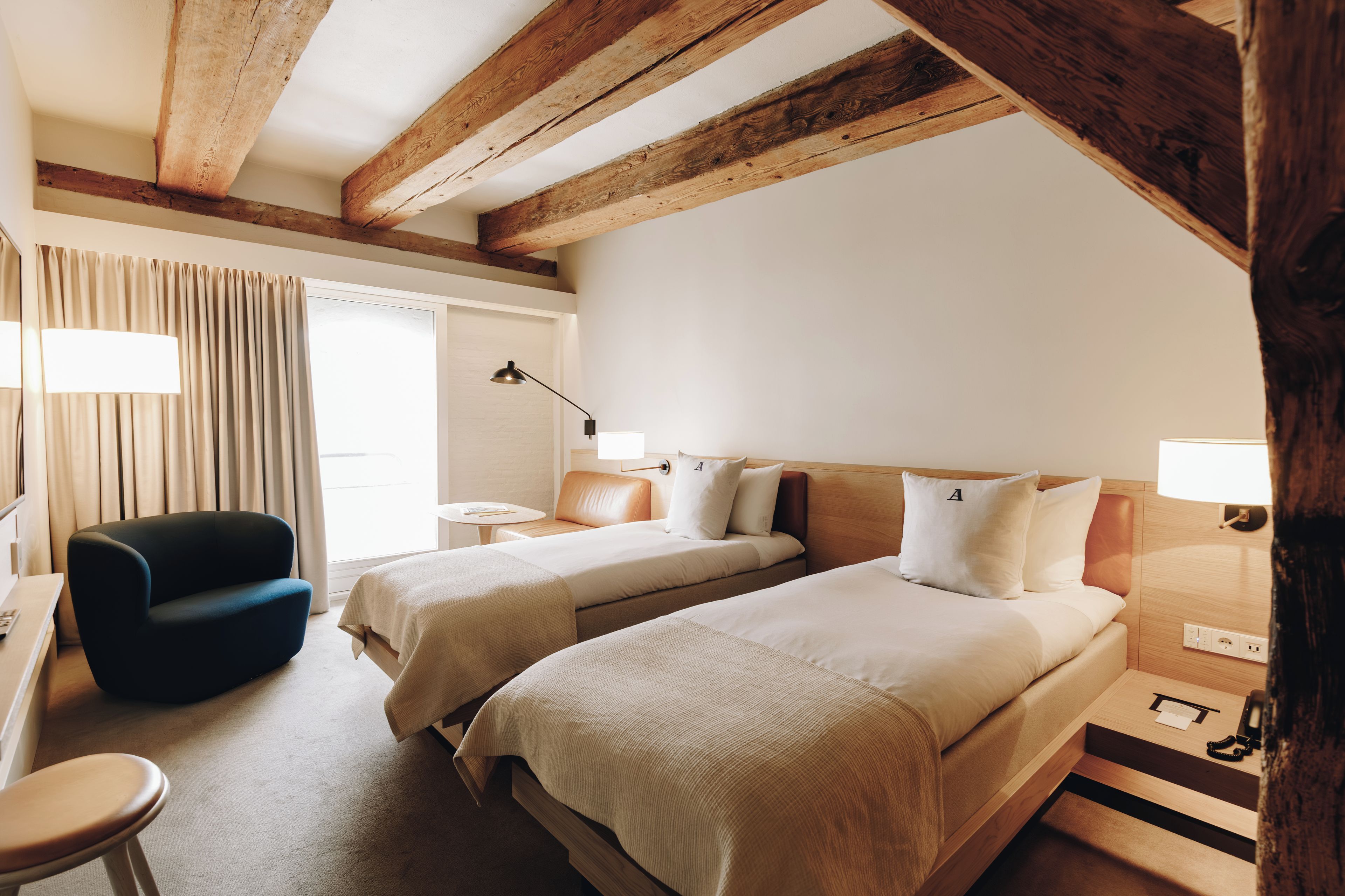 Ett hotellrum med två sängar, ett skrivbord, en stol och ett fönster med gardiner.