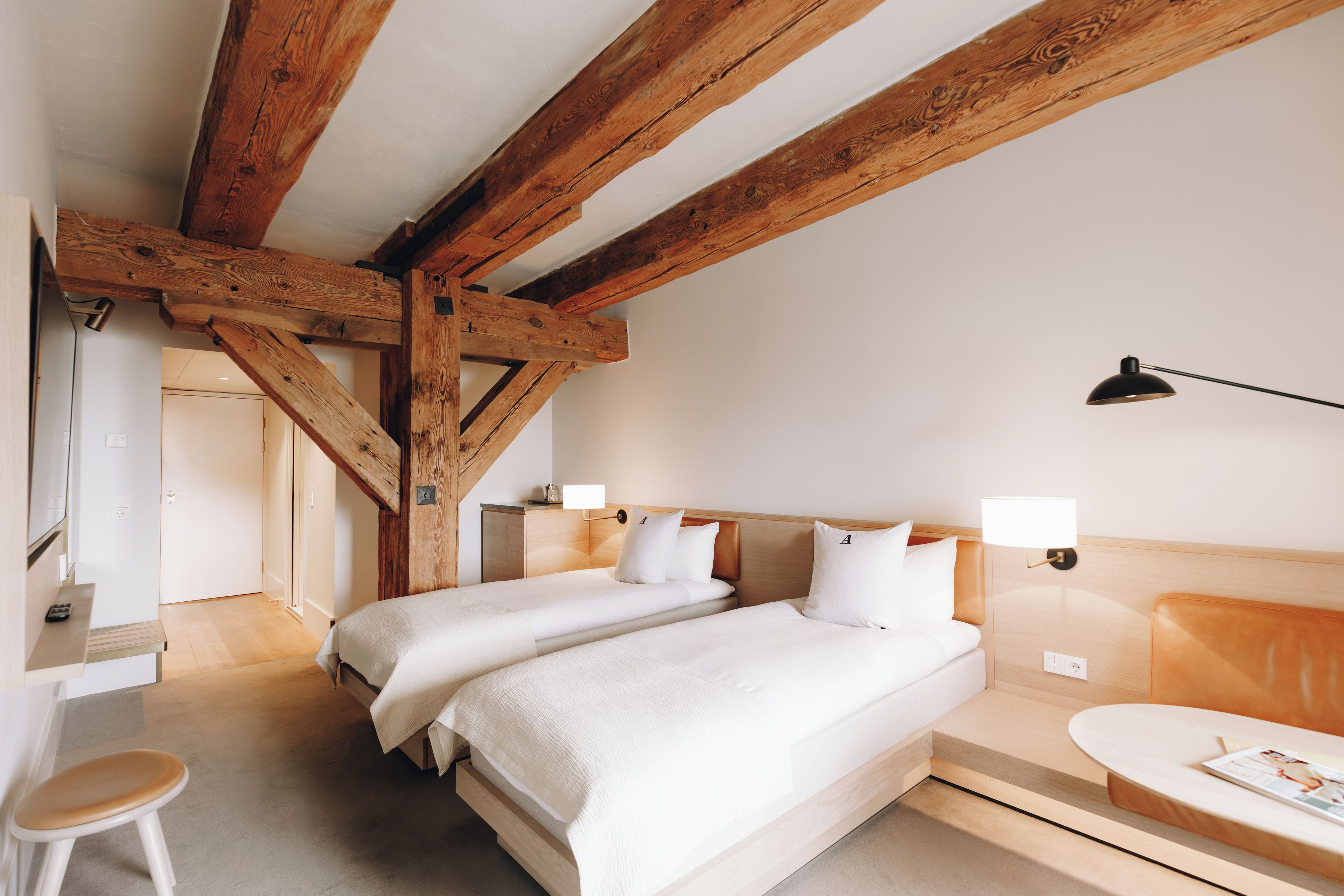 Habitación de hotel con dos camas, vigas de madera, un escritorio y una silla.