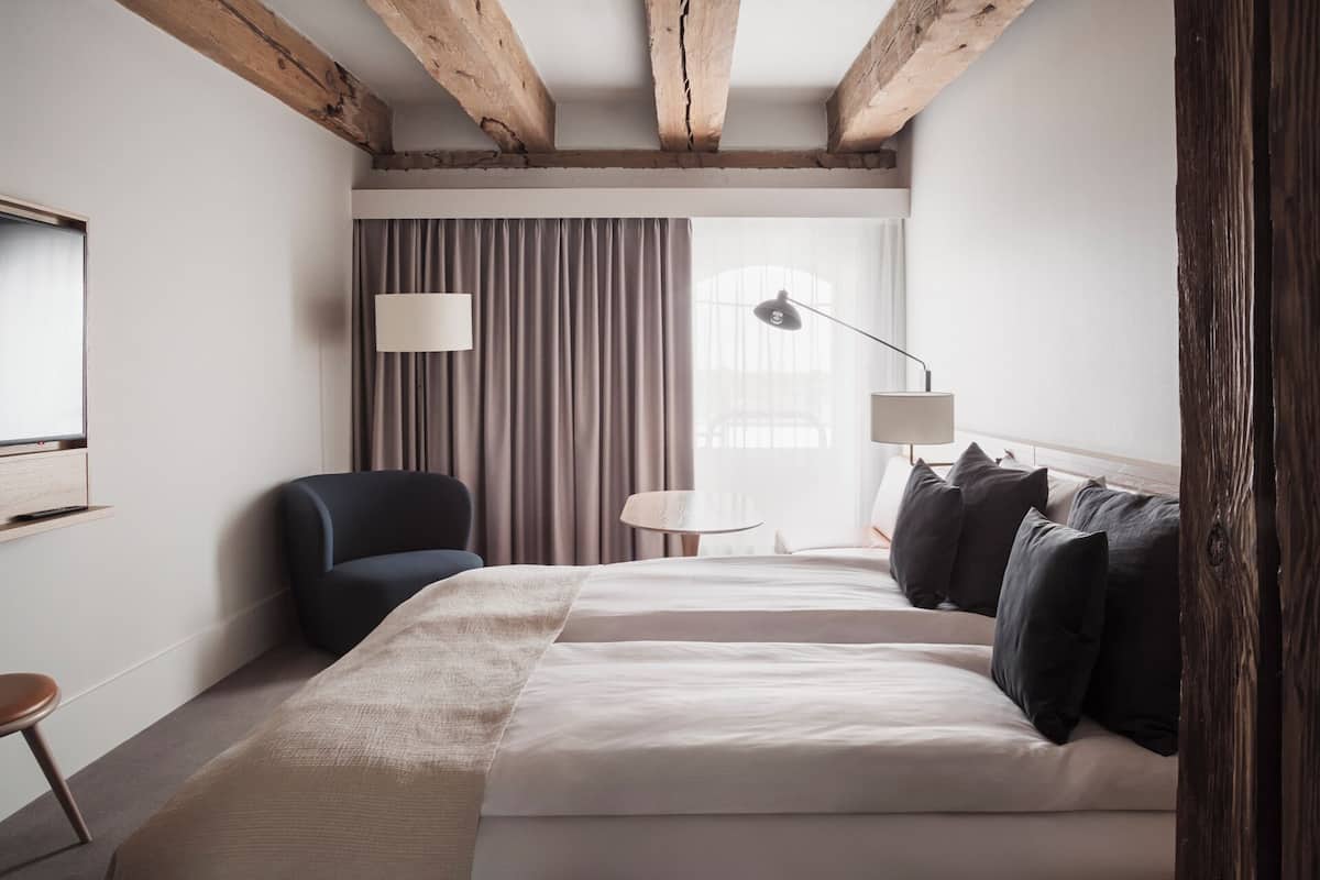 Quarto de hotel com uma cama grande, uma cadeira, uma escrivaninha e um abajur.
