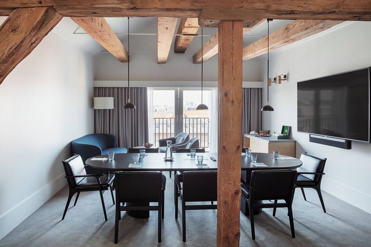 Quarto de hotel moderno com área de refeições, uma televisão grande e varanda com cortinas.