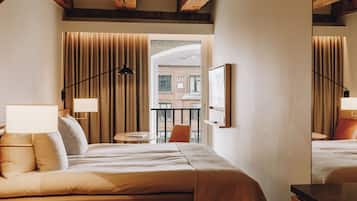 A hotel room with a bed, a desk, a chair, a window with curtains, and a view of a building outside.