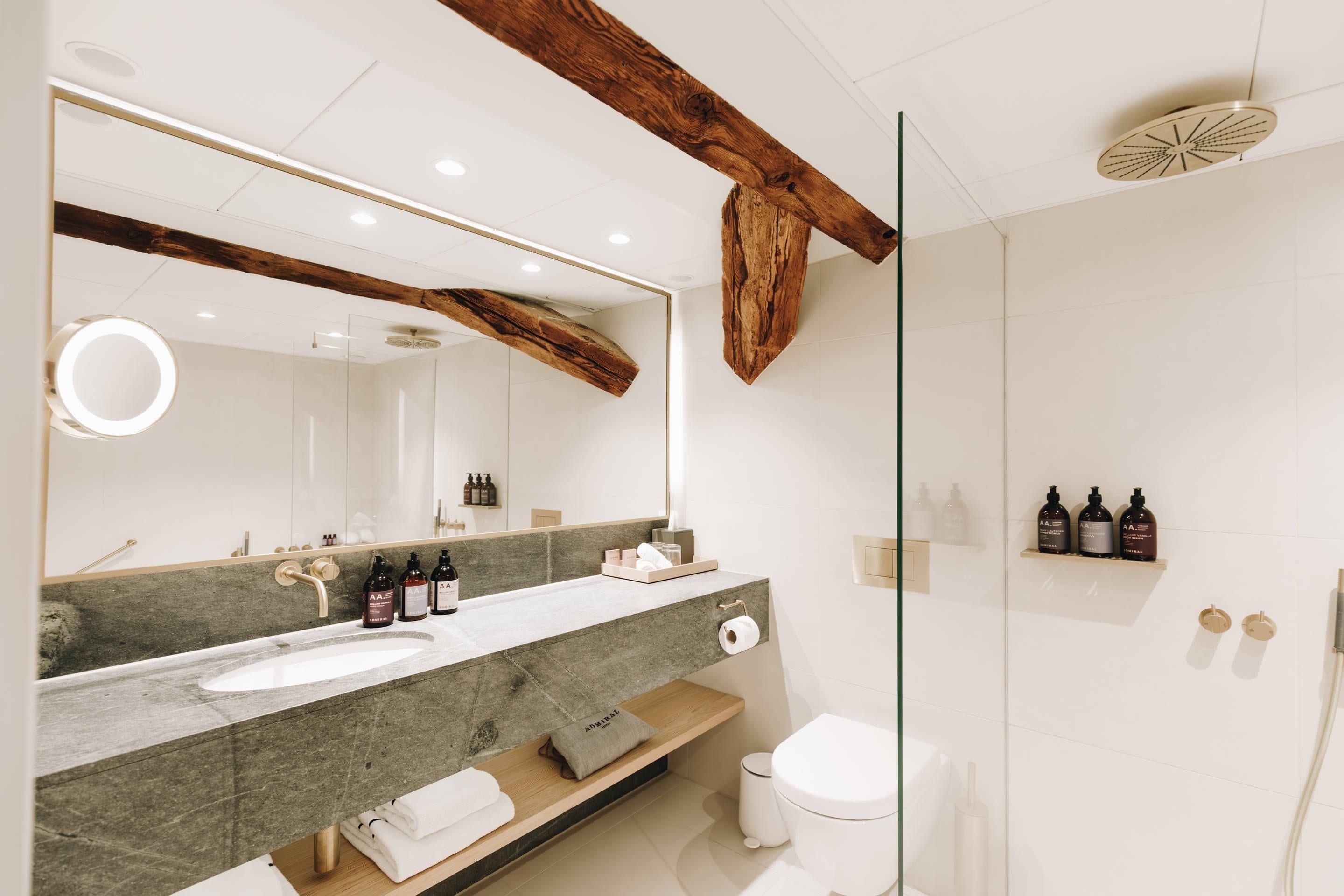 A modern bathroom with a large mirror, a wooden beam ceiling, and a marble countertop.