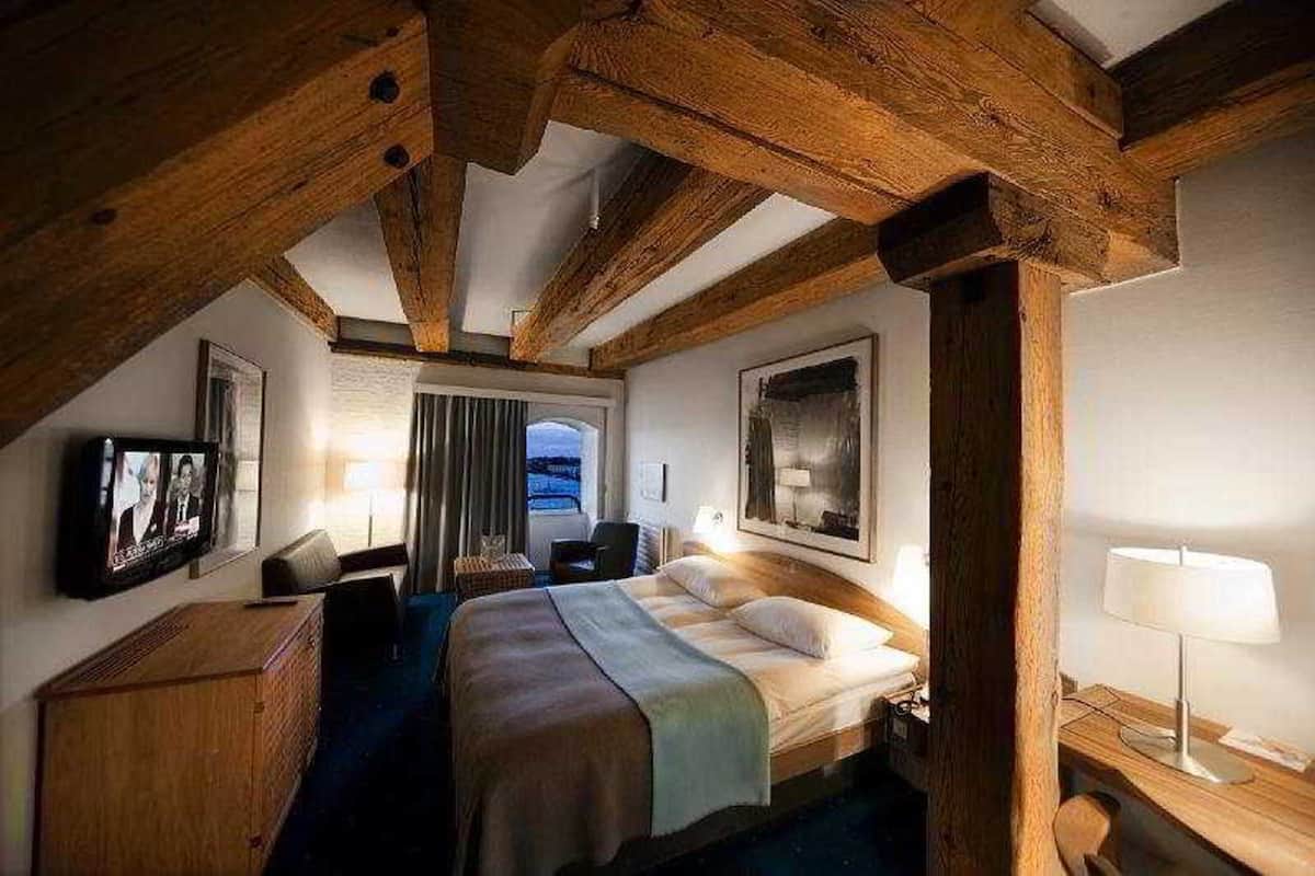 Um quarto com cama, escrivaninha, cadeira, televisão e janela.