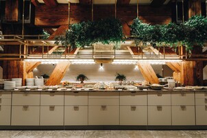 A buffet setup with multiple serving stations, wooden beams, and hanging plants.