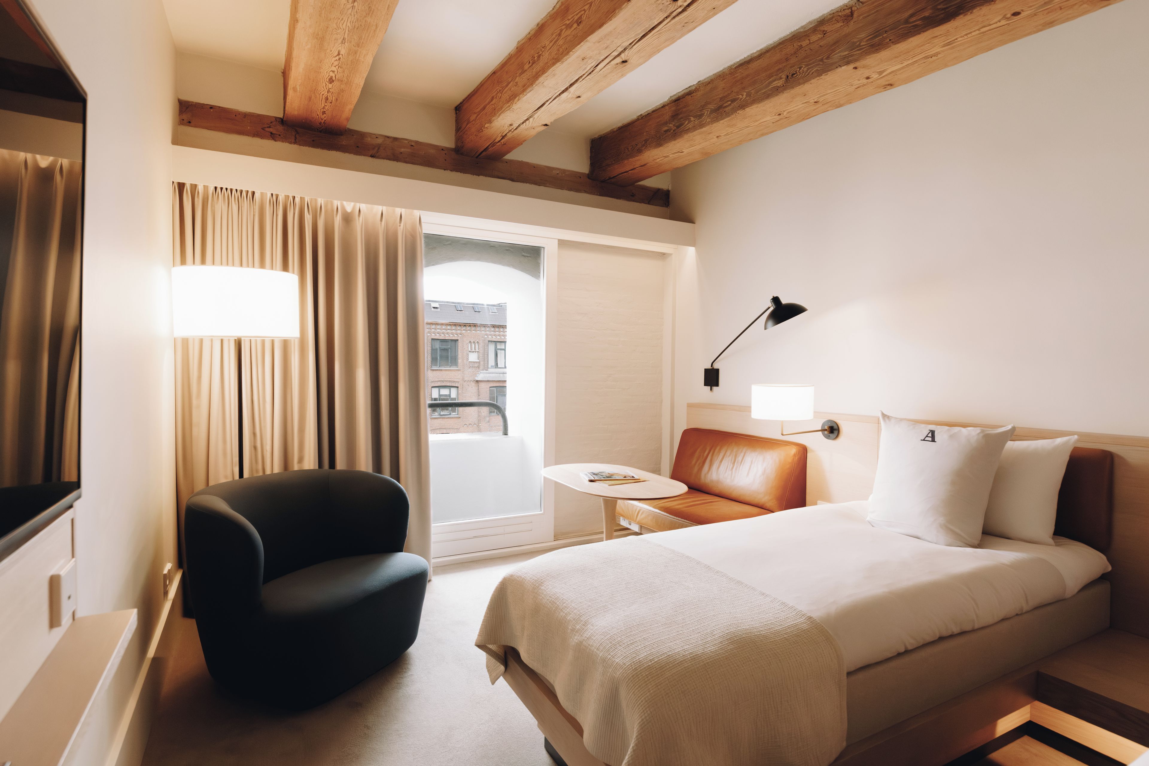 Ett hotellrum med en säng, en stol, ett litet bord, en lampa och utsikt över omgivningarna.