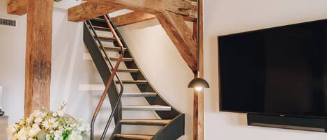 A modern interior with a wooden staircase, a flat-screen TV, and a dining area with a table and chairs.