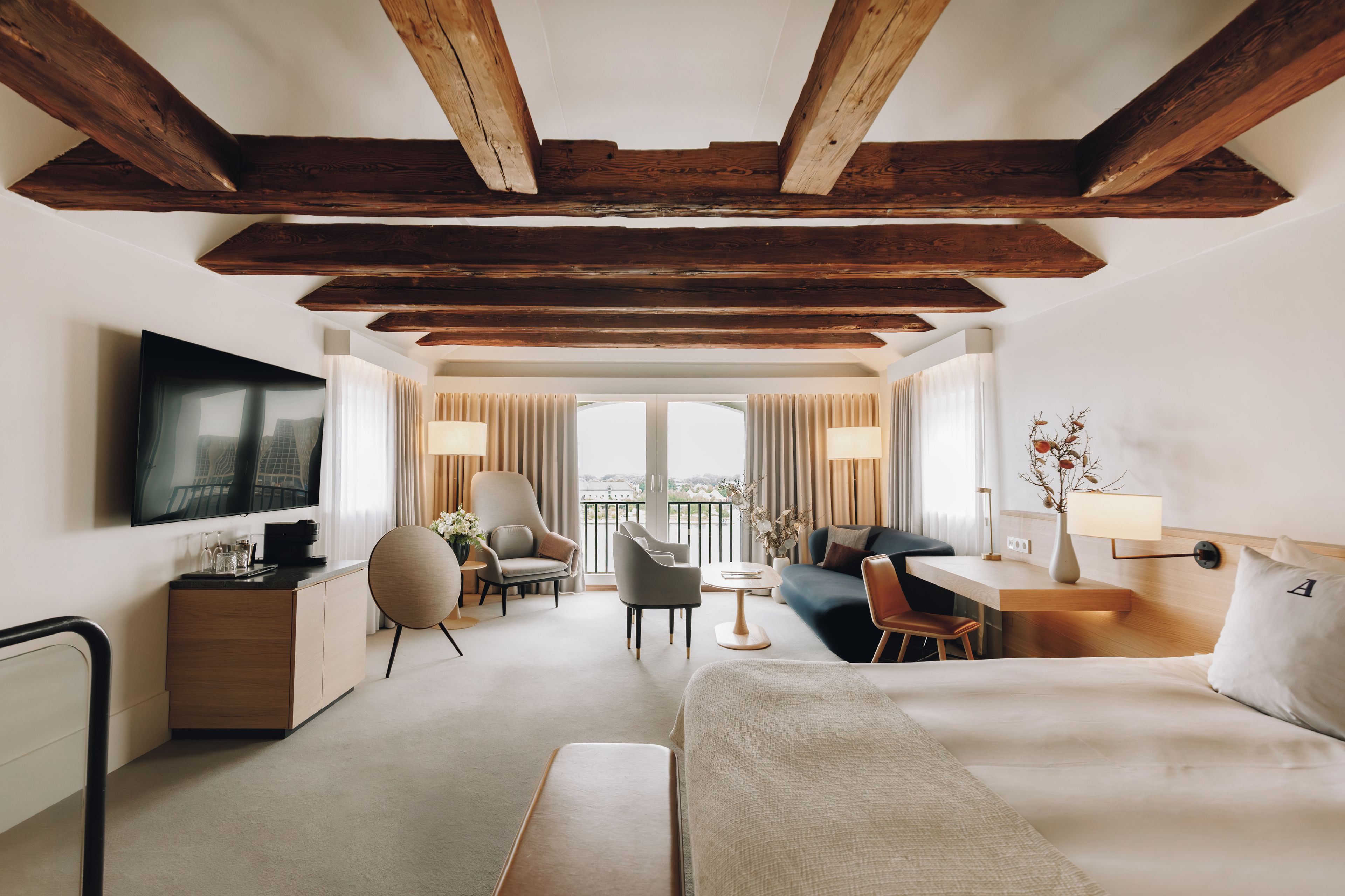 A modern hotel room with a large bed, a sofa, a desk, and a TV.