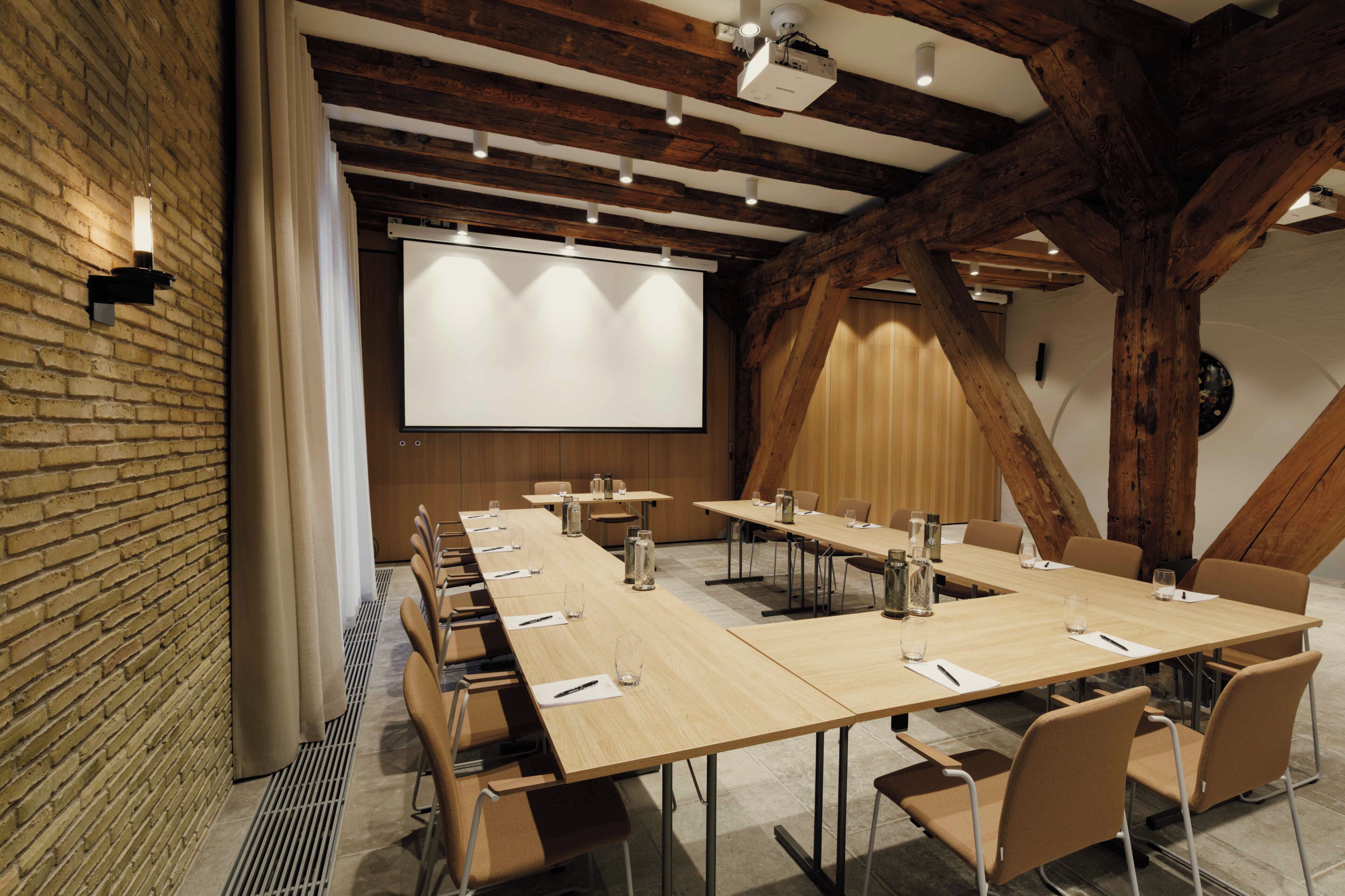 A conference room with a long table, chairs, a projector screen, and wooden beams.