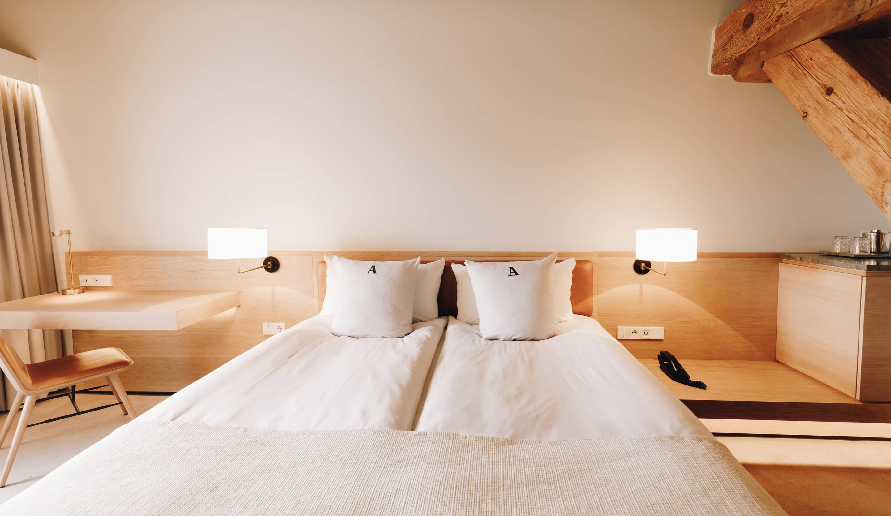 A hotel room with a bed, bedside tables, a desk, a chair, and a telephone.