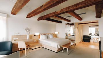 A modern hotel room with exposed wooden beams, a large bed, a desk, and a seating area.