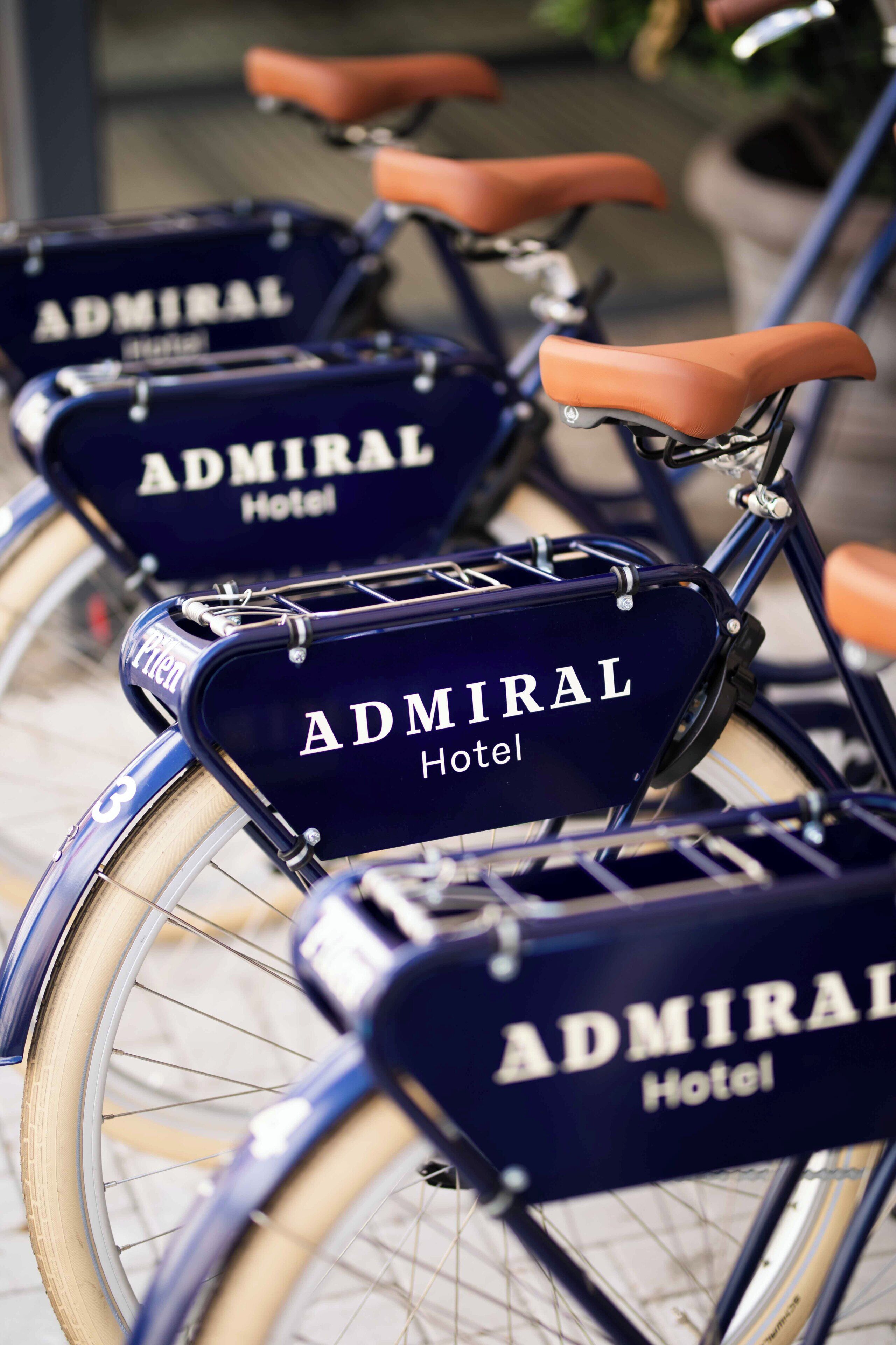 Una fila de bicicletas con el rótulo 'Admiral Hotel', equipadas con sillines y cestas.