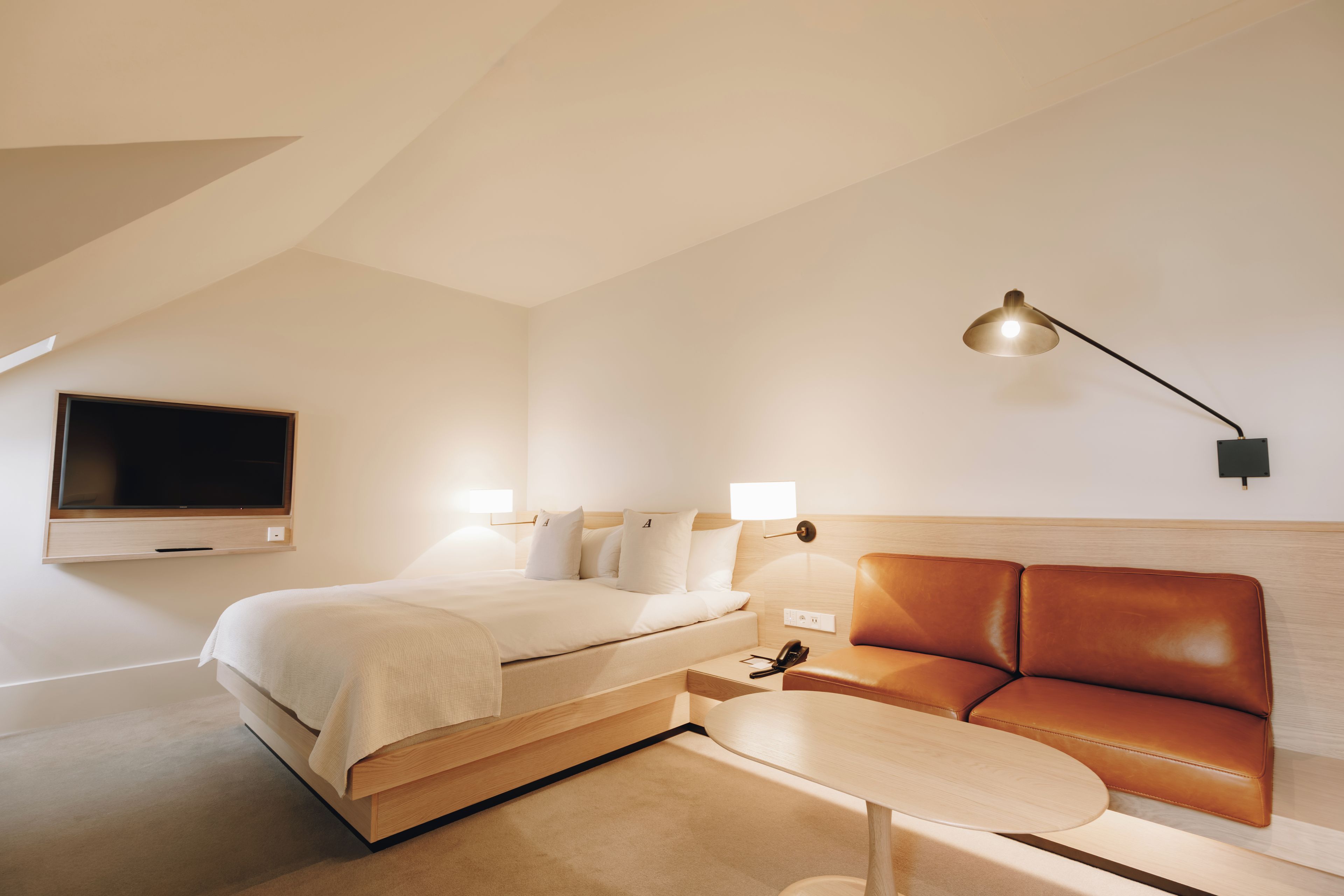A modern hotel room with a bed, a television, a desk, and a leather sofa.