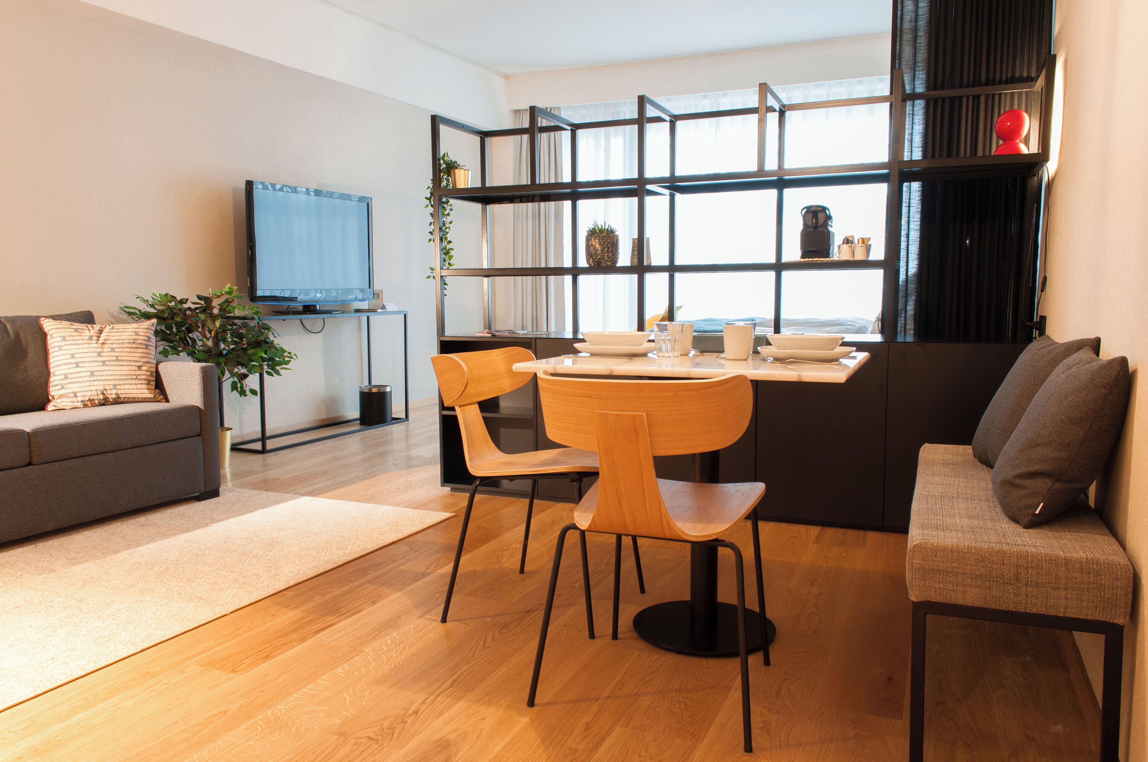 A modern living room with a sofa, a dining table with chairs, a TV, and a bookshelf.