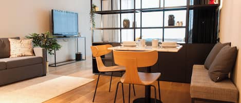 A modern living room with a sofa, a dining table with chairs, a TV, and a bookshelf.