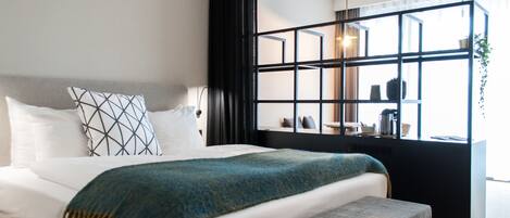 Un dormitorio moderno con una cama grande, un banco, una ventana con vistas y un estante de marco negro con objetos.