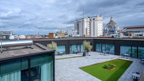 A rooftop terrace with a small lawn, seating area, and a view of surrounding buildings. - PREMIER SUITES PLUS Antwerp (Antwerp)