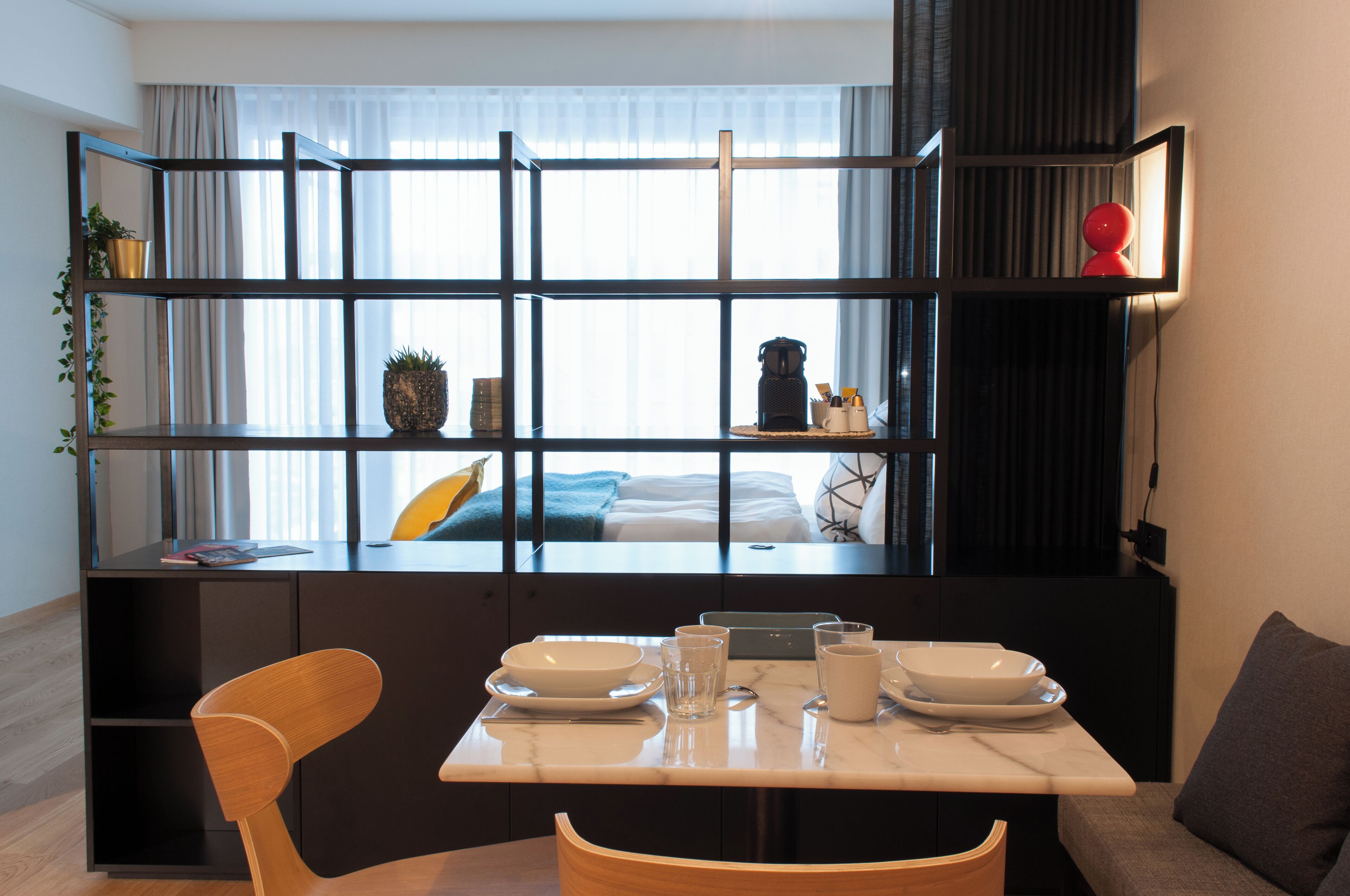 A modern hotel room with a dining area, a sofa, and a large window with curtains.