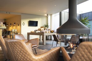A modern dining area with a central table, chairs, and a fireplace. - PREMIER SUITES PLUS Antwerp (Antwerp)