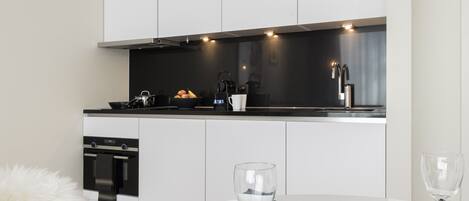 A modern kitchen with white cabinets, a black countertop, and stainless steel appliances. There is a dining table with plates and glasses.