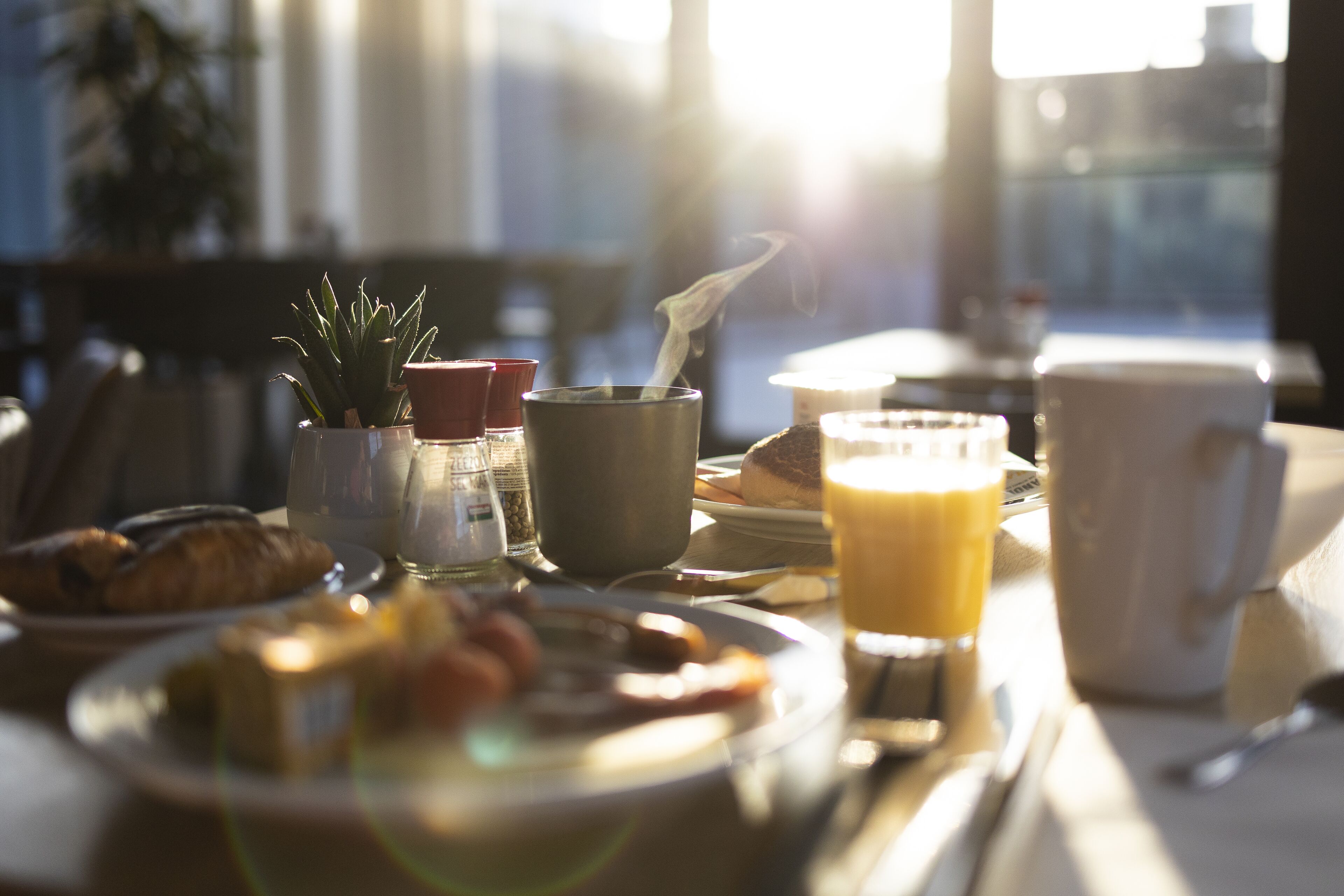 Una mesa de desayuno con diferentes platos, una taza de café y un vaso de zumo de naranja.