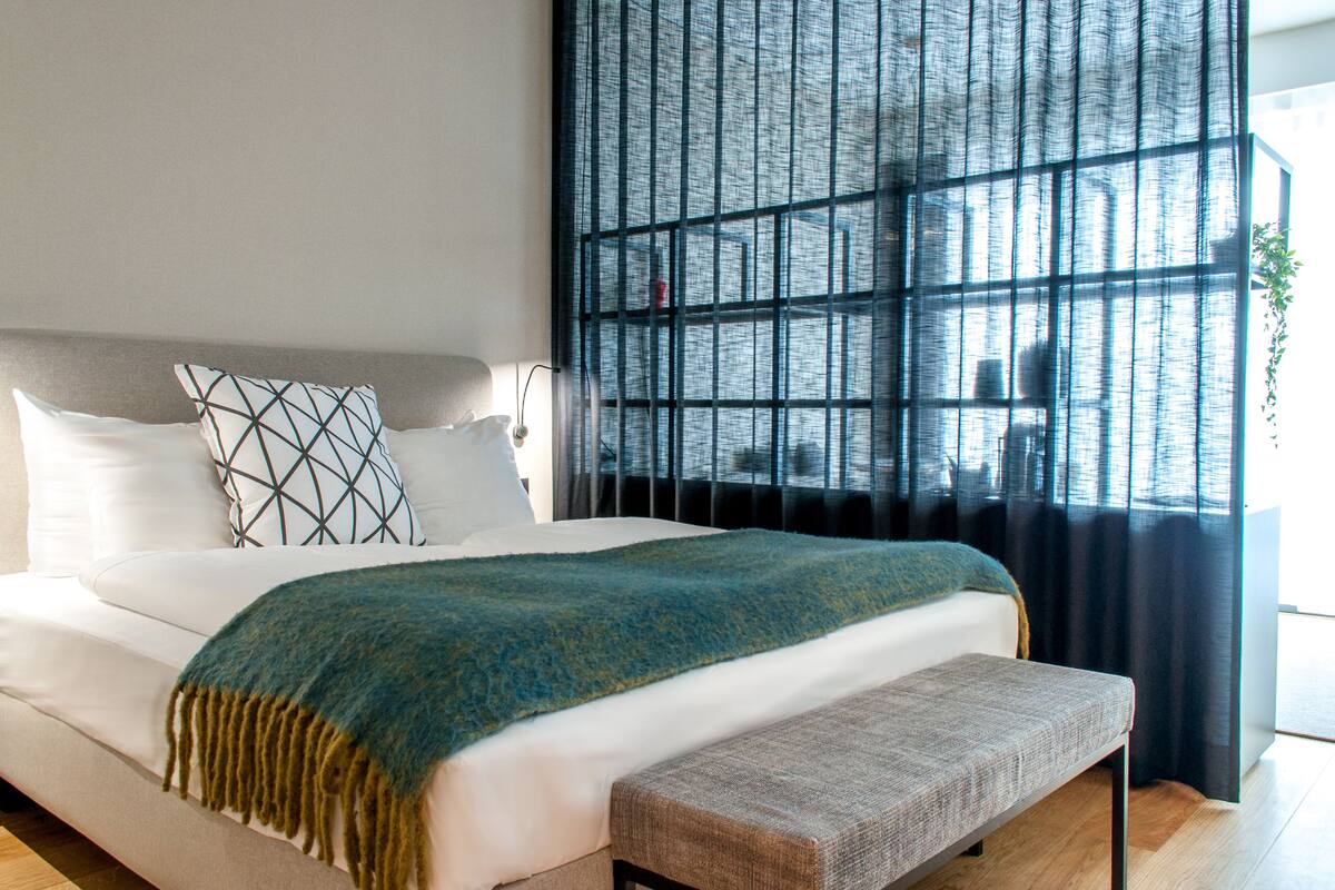 A modern bedroom with a large bed, a bench, and a window with a view of a building.