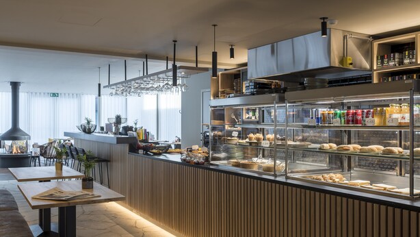 A modern cafe with a wooden counter, glass display case with pastries, and seating area with tables and chairs. - PREMIER SUITES PLUS Antwerp (Antwerp)