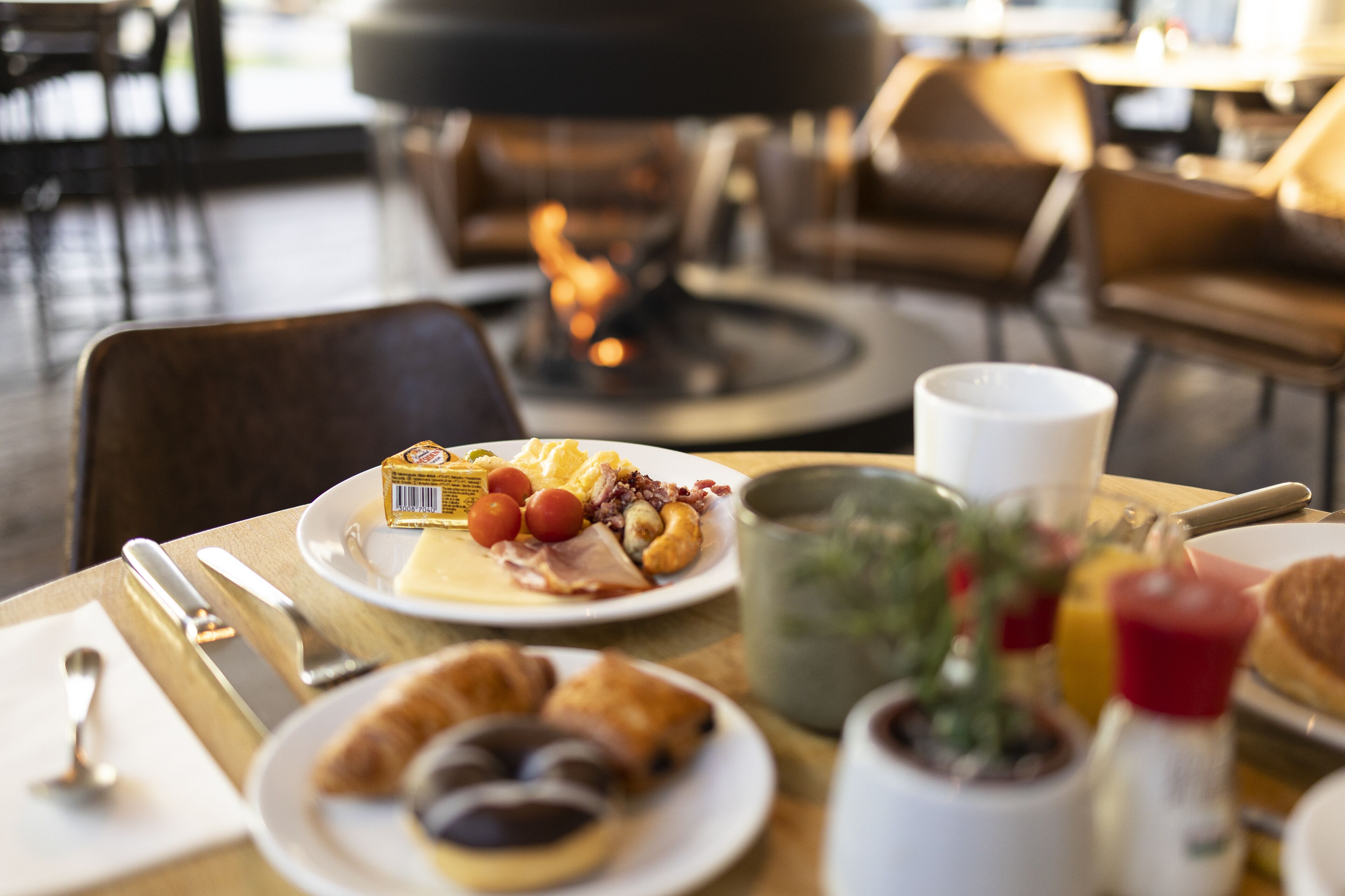 A breakfast setting with a plate of eggs, bacon, and tomatoes, a croissant, and a coffee cup on a wooden table.
