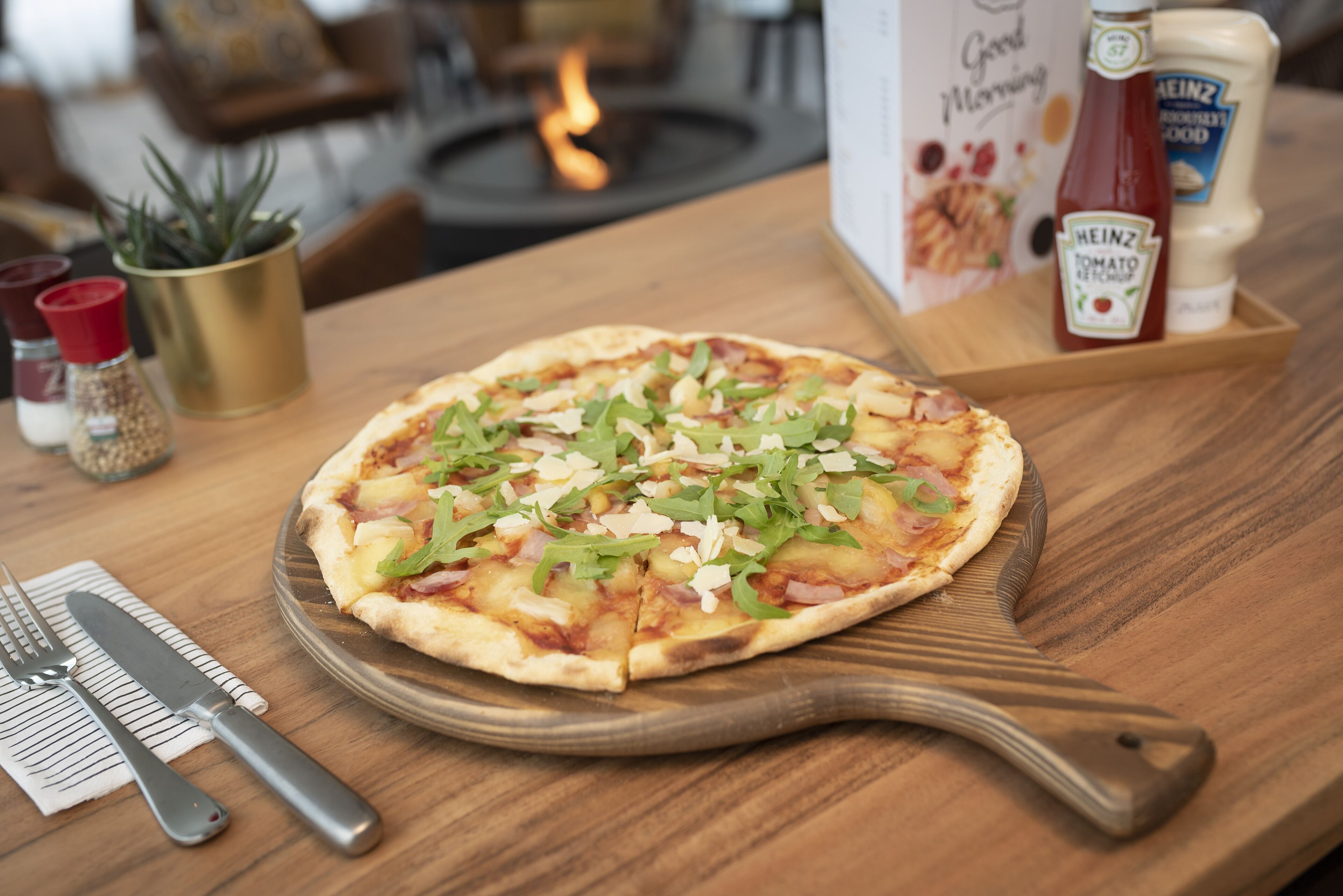 A pizza on a wooden board with a knife and fork beside it.