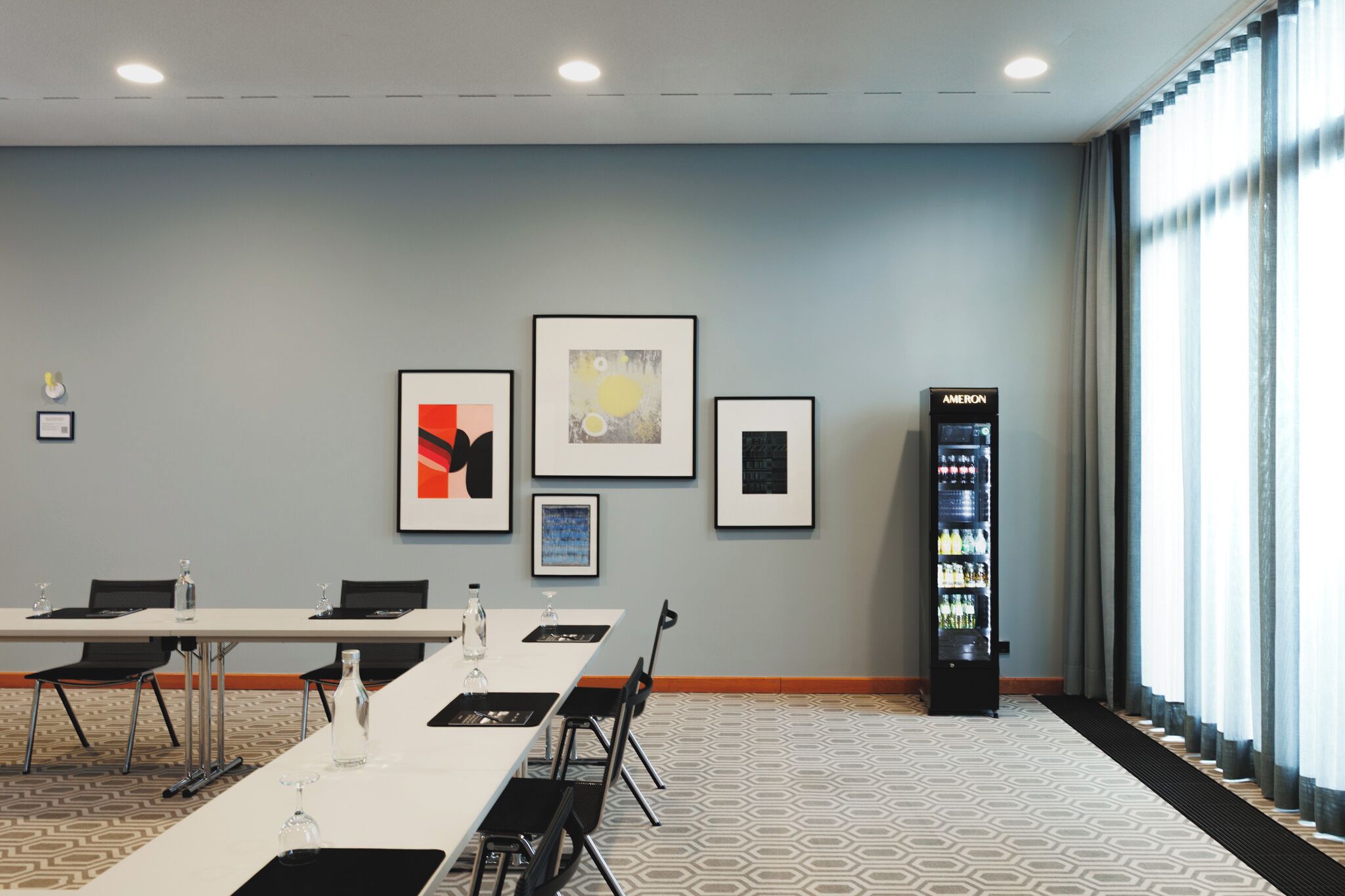 A conference room with a long table, chairs, framed artwork on the wall, and a vending machine.