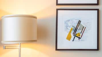 Une lampe moderne dotée d’un abat-jour cylindrique, posée sur une table en bois, deux œuvres d’art abstraites encadrées accrochées au mur et un fauteuil jaune recouvert de tissu.