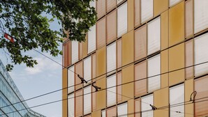A modern building with a prominent 'AMERON' sign, a covered outdoor seating area, and flags on flagpoles. - AMERON Köln Hotel Regent (Cologne)
