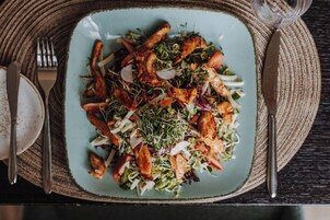Un plato de comida con diversos ingredientes, entre ellos verduras de hoja, carnes y vegetales, sobre un tapete texturizado.