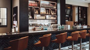 A bar area with multiple shelves of liquor bottles, a bar counter, and several bar stools. - AMERON Köln Hotel Regent (Cologne)